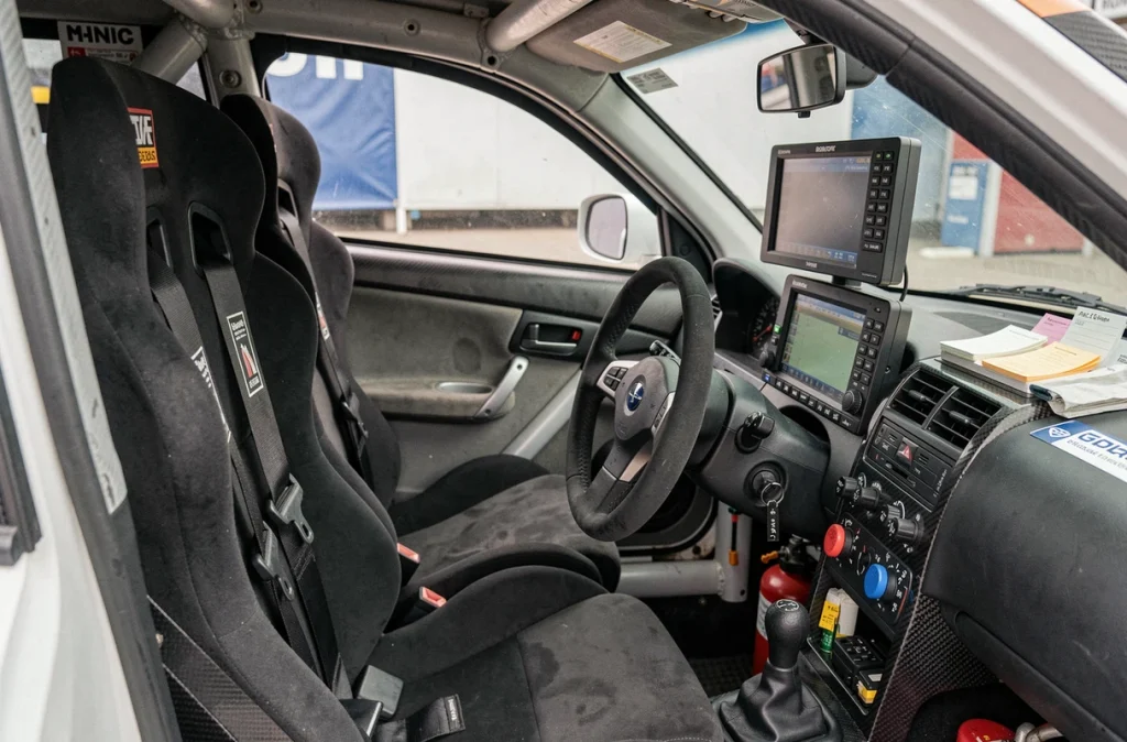 Intérieur du cockpit d'une Subaru WRC avec harnais, arceau de sécurité, volant à commandes et ordinateur de bord de rallye